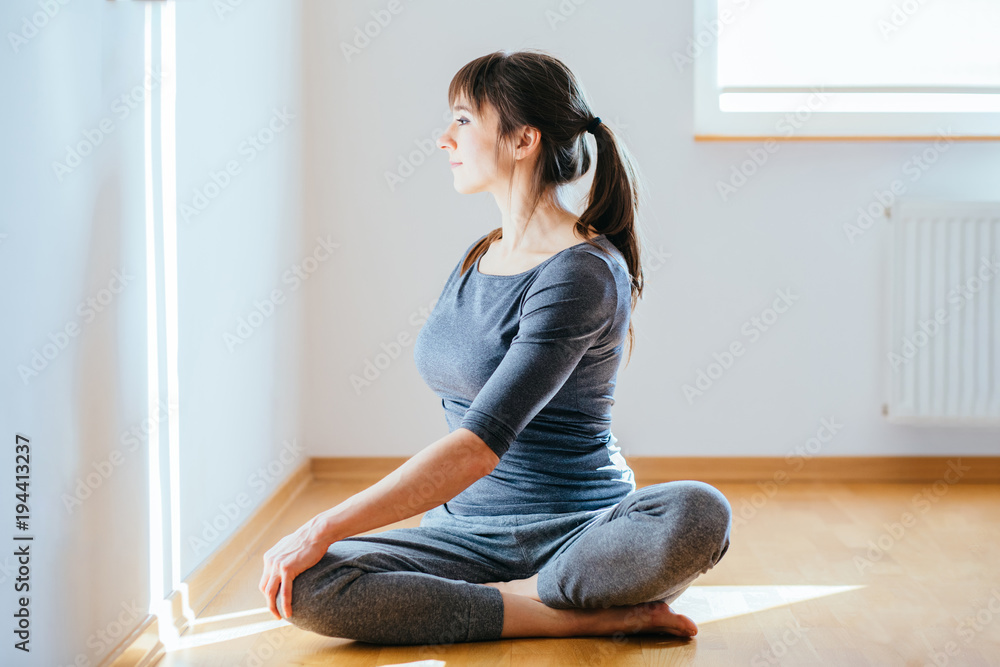 Front view full body portrait of a relaxed candid caucasian woman practicing yoga sitting on the floor in the empty living room at home. New day, morning routine concept.
