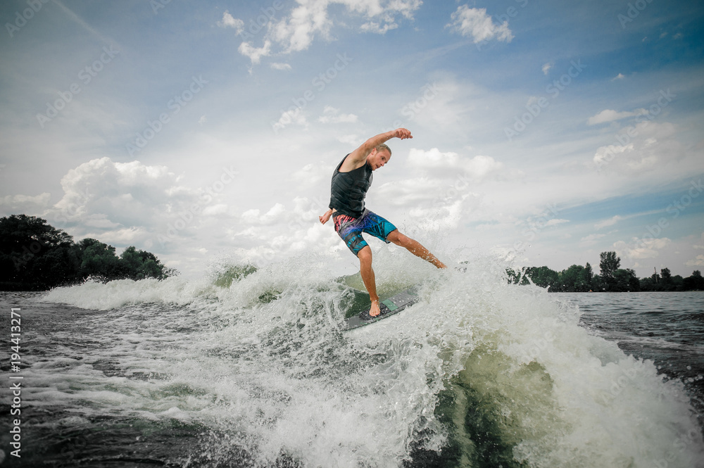 Athletic guy wakesurfing on the board down the river against the sky Athletic guy wakesurfing on the board down the river against the sky