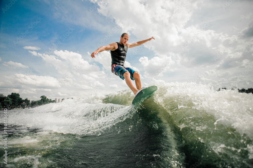Young and active man wakesurfing on the board down the river - obrazy, fototapety, plakaty 