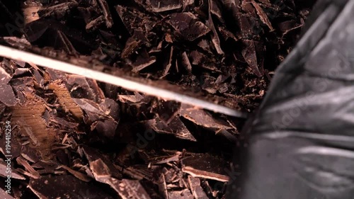 Chopping chocolate on cutting board on wooden table as baking ingredient preparation (slow motion) photo