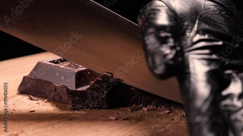 Chopping chocolate on cutting board on wooden table as baking ingredient preparation (slow motion) photo