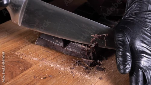 Chopping chocolate on cutting board on wooden table as baking ingredient preparation (slow motion) photo