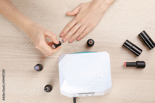 Woman making manicure near ultraviolet lamp on table
