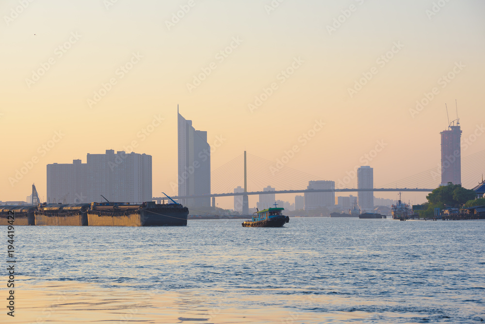 Tugboat take barges downstream on the river to the sea under the sunset in the city.