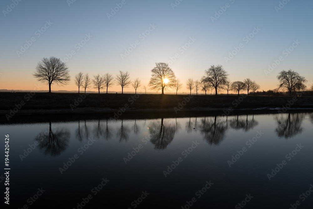 Morning sunrise Backlight behind winter trees by the shore 