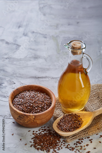 Flax seeds in bowl and flaxseed oil in glass bottle on light textured background, top view, close-up, selective focus