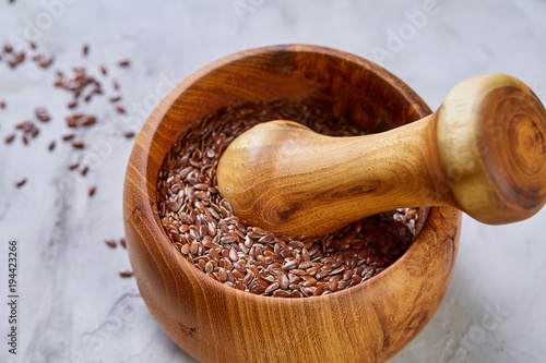 Top view close-up picture of wooden pestle and mortar with flaxseeds on light background, shallow depth of field