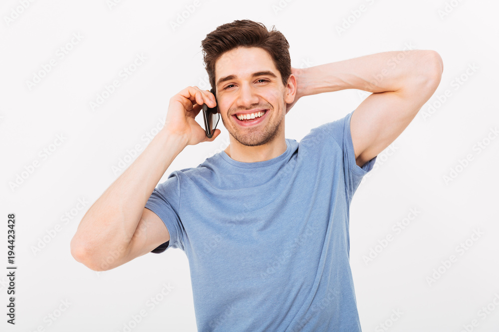 Smiling man in t-shirt talking by smartphone while holding head Smiling man in t-shirt talking by smartphone while holding head