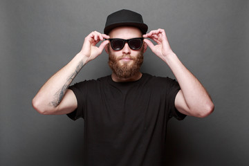 Hipster handsome male model with beard wearing black blank t-shirt with space for your logo or design over gray background