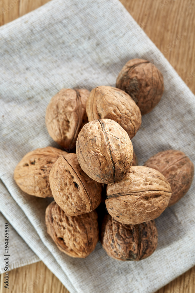 A stack of hard shells of walnuts piled together on light grey fabric cotton tablecloth, selective focus A stack of hard shells of walnuts piled together on light grey fabric cotton tablecloth, selective focus