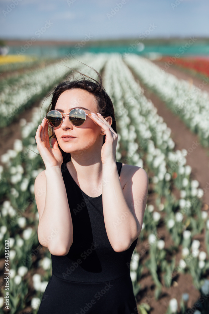 Young Woman in sunglasses in Spring sunny day on tulips Flower field. Mother's Day. Springtime Young Woman in sunglasses in Spring sunny day on tulips Flower field. Mother's Day. Springtime