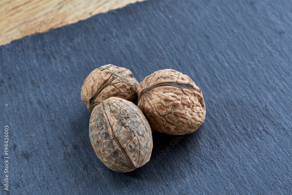 A stack of hard shells of walnuts piled together on dark piece of wood, selective focus A stack of hard shells of walnuts piled together on dark piece of wood, selective focus