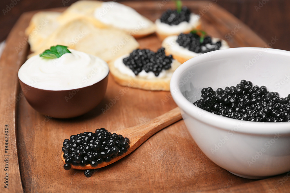 Bowl and spoon with delicious black caviar on wooden board Bowl and spoon with delicious black caviar on wooden board