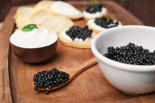 Bowl and spoon with delicious black caviar on wooden board
