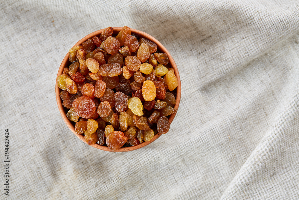 Ceramic bowl with golden raisins on light tablecloth, close-up, selective focus Ceramic bowl with golden raisins on light tablecloth, close-up, selective focus