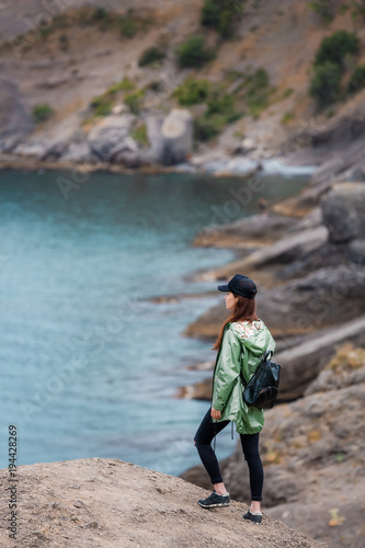 Girl sitting on the rock near to the seaside, resting after hiking. Woman in sportswear, healthy lifestyle. Successful hiker hiking on seaside mountain peak