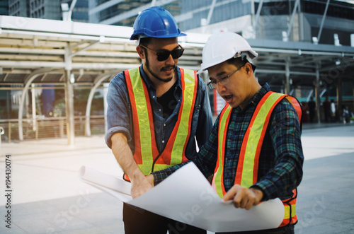 group of engineer, technician and architect with safety helmet planning about building plan with blueprint in modern city building background, construction site, business, industry and worker concept