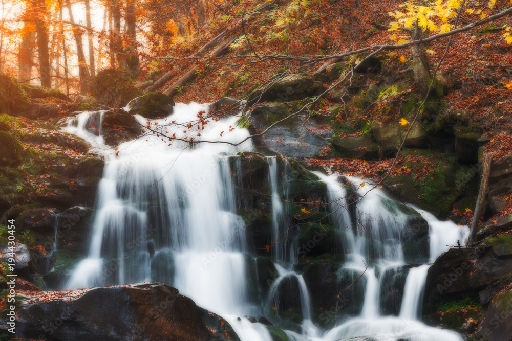 Amazing autumn scenery with yellow leaves on small branch above stream of mountain waterfall. Beautiful nature background.