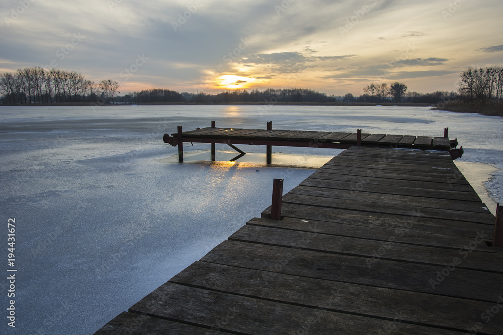 Wooden jetty and frozen lake at sunset