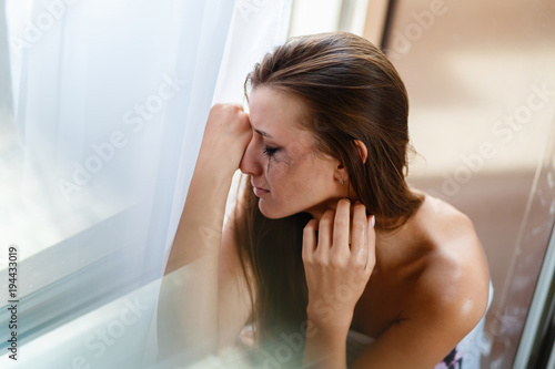 Girl with blurred makeup tears crying in the corner. Depression and stress woman portrait. Broken heart woman crying alone near the window, the concept of Valentine's Day.