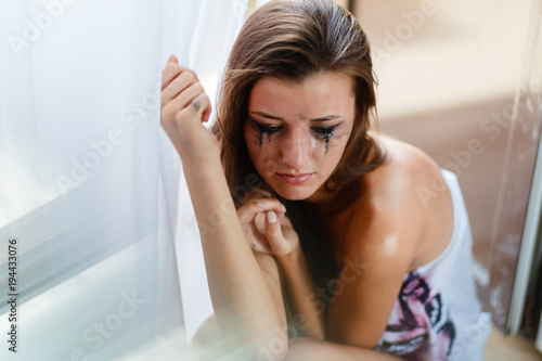 Girl with blurred makeup tears crying in the corner. Depression and stress woman portrait. Broken heart woman crying alone near the window, the concept of Valentine's Day.
