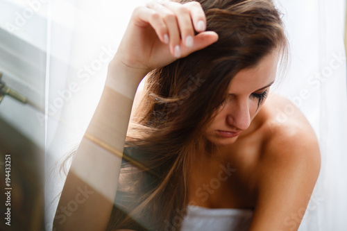 The girl with long hair sitting and crying, smearing mascara and tears on her face. A weeping woman holds her head with her hand in frustration from losing or parting or breaking up a relationship.