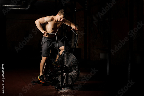 Young and sexy man practicing crossfit using an exercise bike in a gym