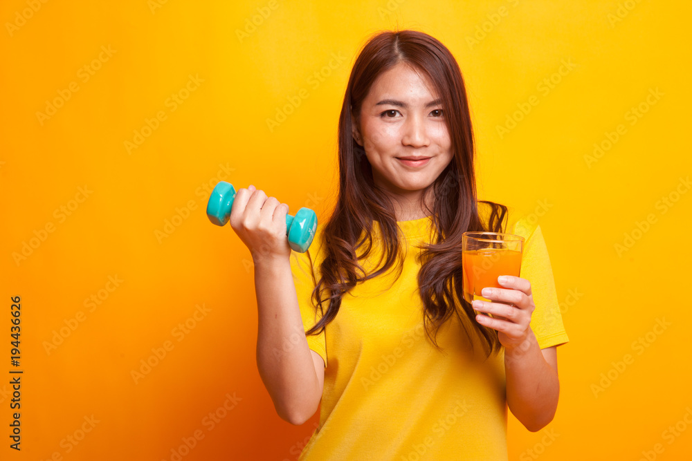 Young Asian woman with dumbbell drink orange juice in yellow dress Young Asian woman with dumbbell drink orange juice in yellow dress