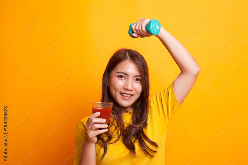 Healthy Asian woman with dumbbell and tomato juice in yellow dress Healthy Asian woman with dumbbell and tomato juice in yellow dress