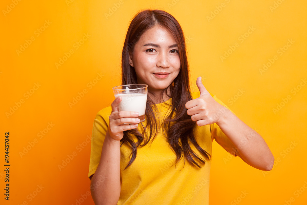 Healthy Asian woman drinking a glass of milk thumbs up in yellow dress Healthy Asian woman drinking a glass of milk thumbs up in yellow dress
