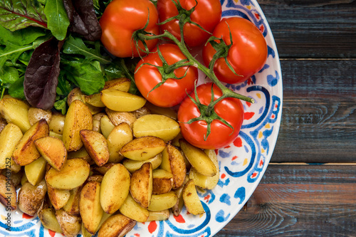 Fried baby potatoes, green salad and fresh tomatoes on a big plate in rustic style