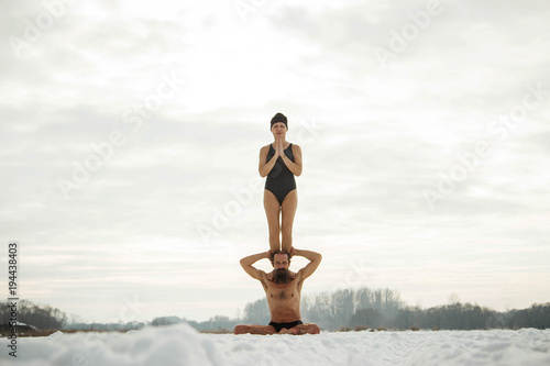 A man and a middle-aged woman practicing yoga on a frozen river. A pair of yoga. © ferkhova