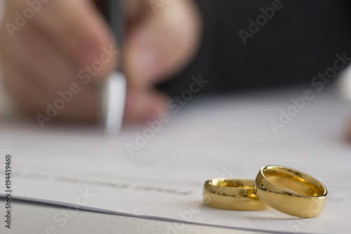 Hands of wife, husband signing decree of divorce, dissolution, canceling marriage, legal separation documents, filing divorce papers or premarital agreement prepared by lawyer. Wedding ring photo