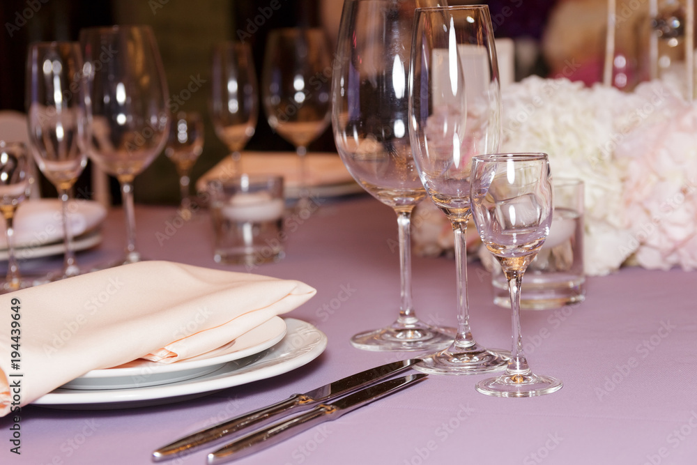 A stylish wedding decor of dishes, white bouquets with flowers, candles and glasses stand on a light tablecloth of a served table. Side view, selective focus