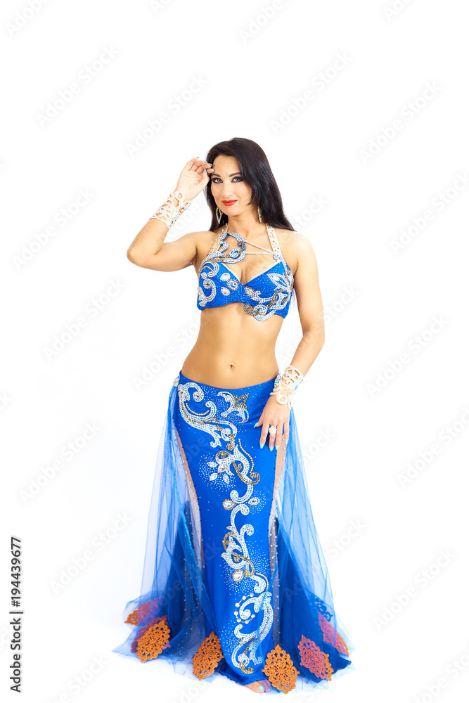 A young dancer in blue clothes performs an oriental belly dance. Isolate. Beautiful girl in bright national clothes dancing on white background. A young dancer in blue clothes performs an oriental belly dance. Isolate. Beautiful girl in bright national clothes dancing on white background.