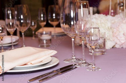 A stylish wedding decor of dishes  white bouquets with flowers  candles and glasses stand on a light tablecloth of a served table. Side view  selective focus