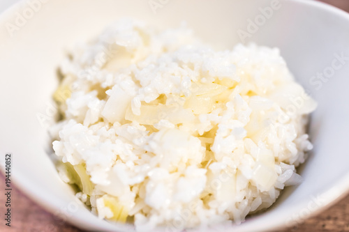 Macro closeup of cooked sticky sweet glutinous medium grain rice in white bowl with fresh yellow onions on table, detail, texture