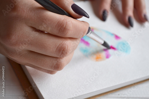 Woman paints in a sketchbook. Tools for painting on the white wooden desk. Painter work.