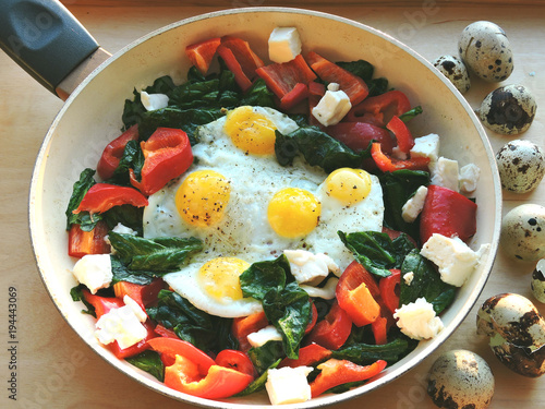 Appetizing fried quail eggs with spinach, feta cheese and peppers.