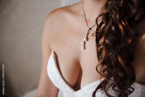 Bust of the bride. An open wedding dress with bare shoulders. Decoration on the neck. Wedding details.