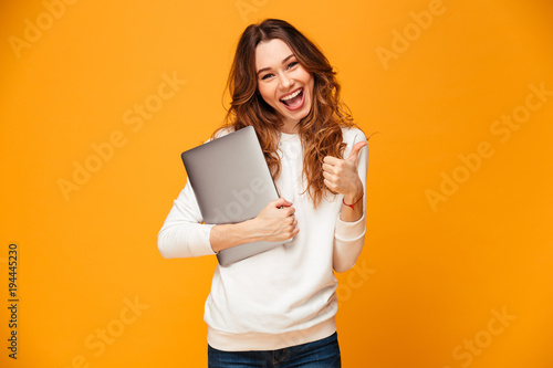 Cheerful young woman holding laptop computer showing thumbs up.
