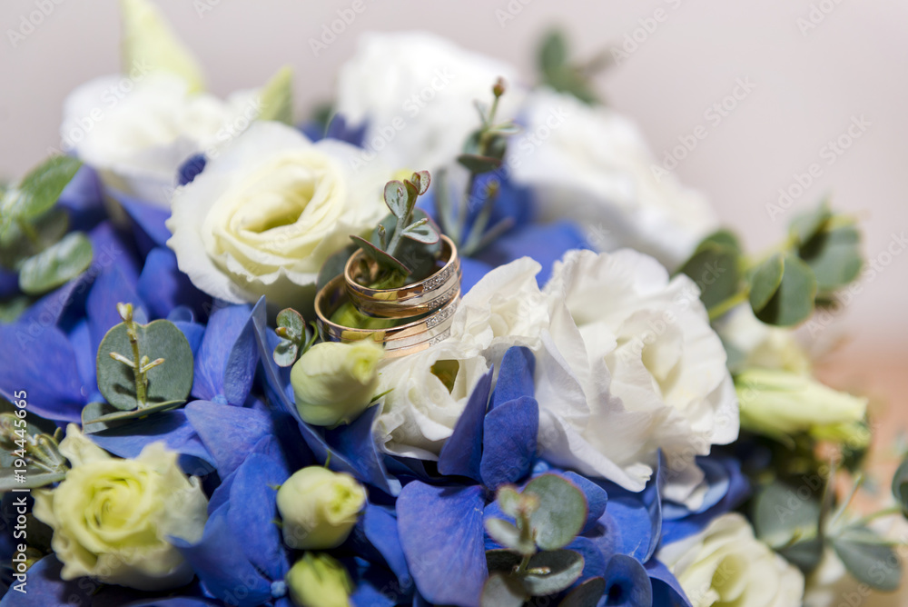 gold wedding rings on a bouquet of white and blue flowers gold wedding rings on a bouquet of white and blue flowers