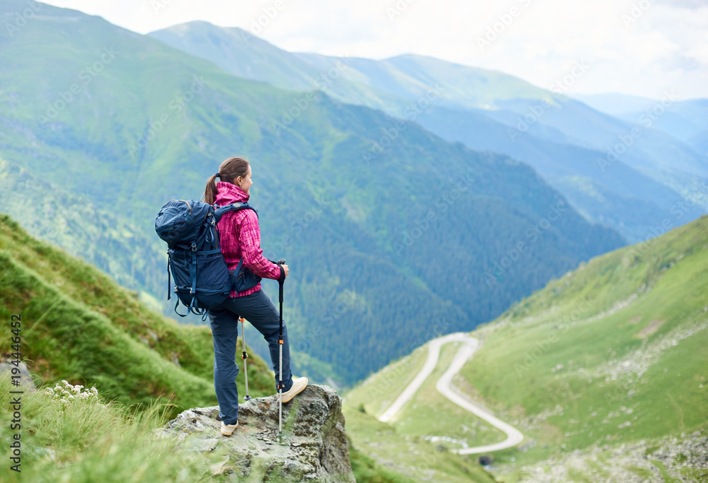 Female traveller with a backpack resting on top of a hill looking away at Transfagarasan road travelling Romania hiking backpacking tourism lifestyle memories harmony destinations active.