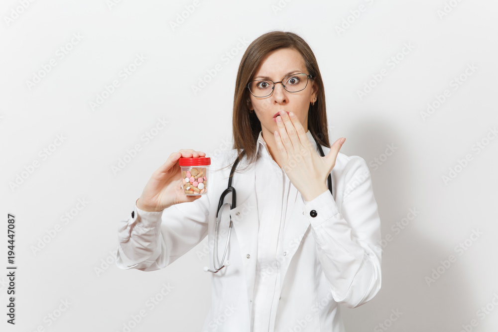 Concerned upset young doctor woman with stethoscope isolated on white background. Female doctor in medical gown holds bottle with pills, put her hand to mouth. Healthcare personnel, medicine concept. Concerned upset young doctor woman with stethoscope isolated on white background. Female doctor in medical gown holds bottle with pills, put her hand to mouth. Healthcare personnel, medicine concept.