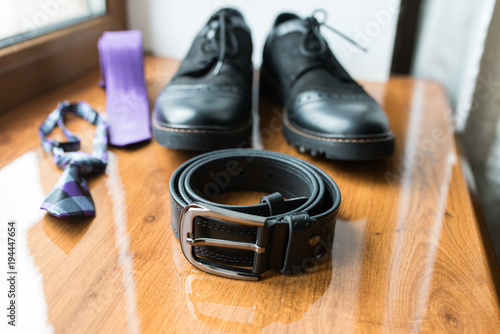 Groom’s accessories: black leather belt in focus, black shoes, necktie. Wedding