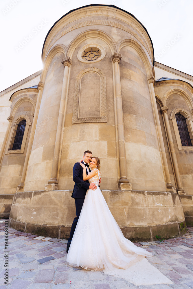 beautiful newlyweds hugging and looking at camera lens against the background of the building