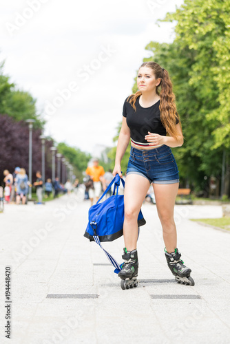 Young woman riding roller skates holding bag