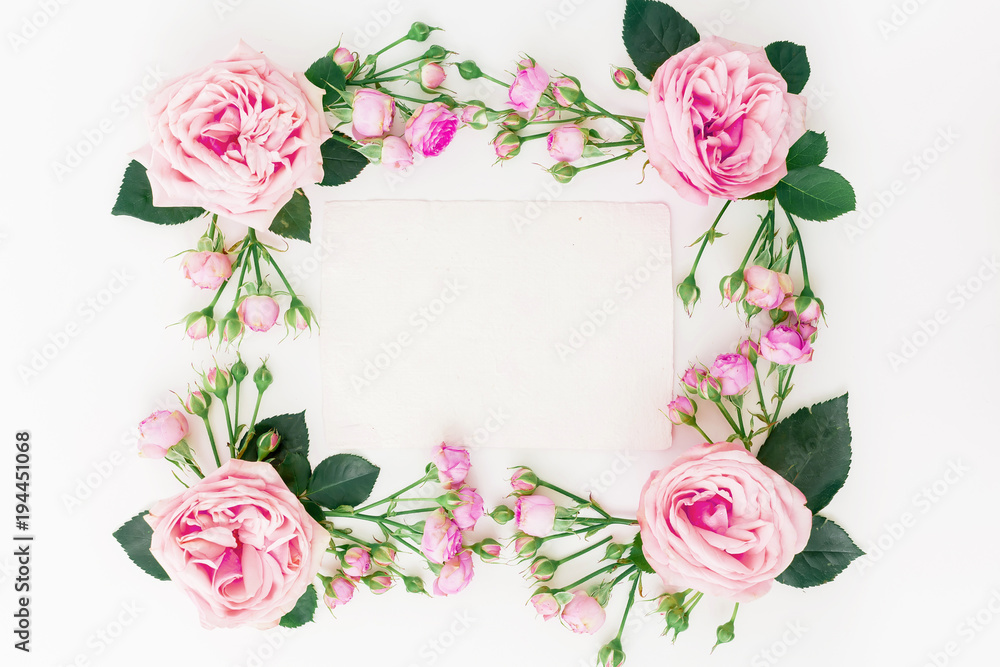 Floral frame with pink roses, buds, leaves and paper card on white background. Flat lay, top view. Spring background