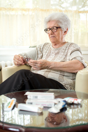 Confused senior woman with eyeglasses reading pill labels.