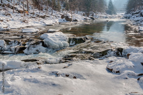 Winter landscape. Mountain river flows from the rocks. Snow and mountain river